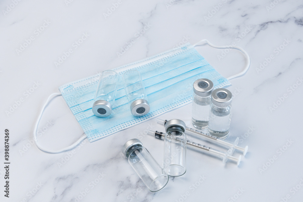Fototapeta premium Two Full and Two Empty Medical Vaccine Ampules and Two Syringes on Marble Counter top along side one medical face masks..