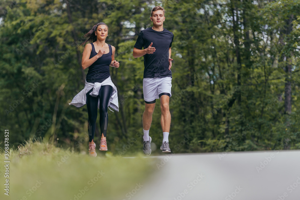 Young fit couple atheltes running on running road in a forest. Young fit couple atheltes running on running road in a forest.