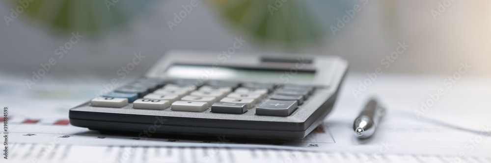 Big gray calculator and black ball pen laying on table and financials papers Big gray calculator and black ball pen laying on table and financials papers