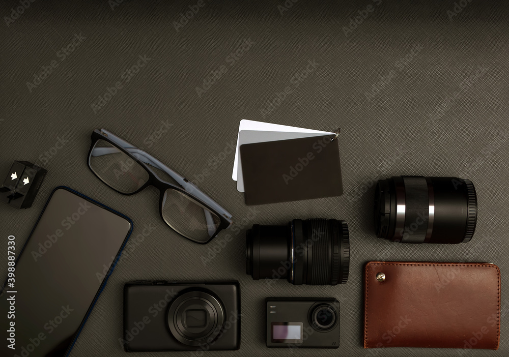 A set of the lens, cameras, smartphone, batteries, a halftone target, glasses and wallet on the dark background. Close-up. Flat lay. Copy space.