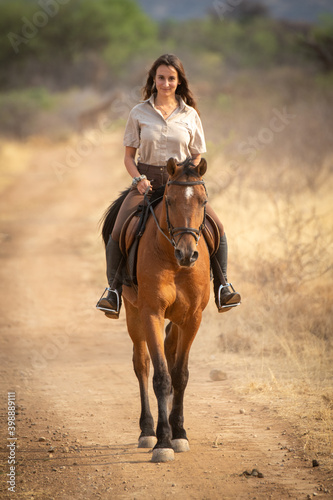 Brunette rides horse on dirt track smiling © Nick Dale