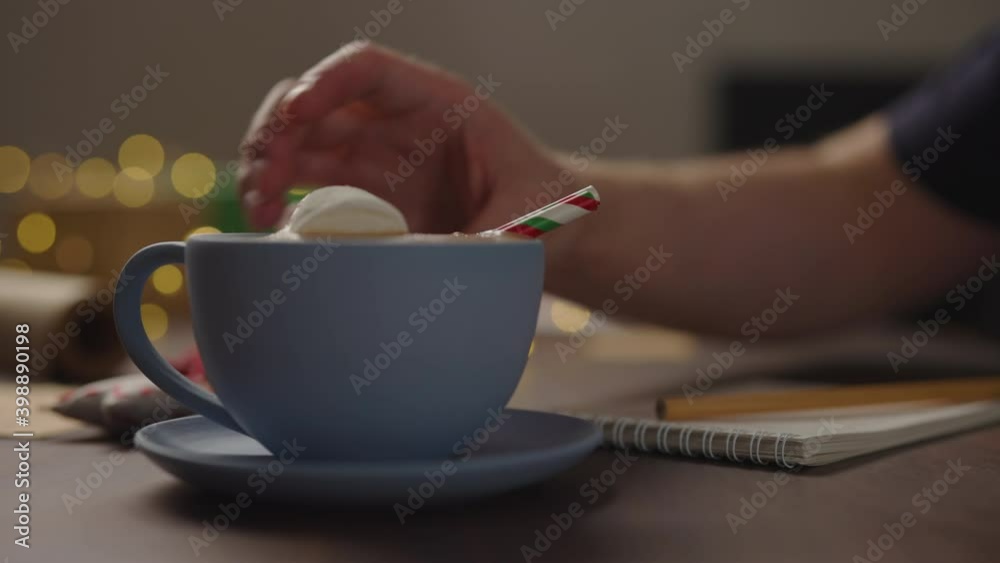 Slow motion orbit shot of man drinking hot chocolate from blue cup in the evening making shopping list for holidays Slow motion orbit shot of man drinking hot chocolate from blue cup in the evening making shopping list for holidays