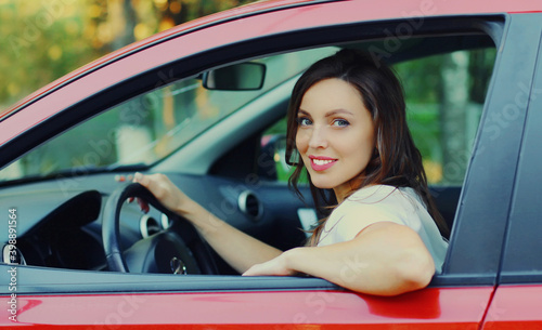 Portrait of happy smiling woman driver behind a wheel red car