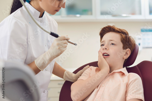 Children dental clinic. Little boy sits in a dentist chair and suffers from severe toothache.