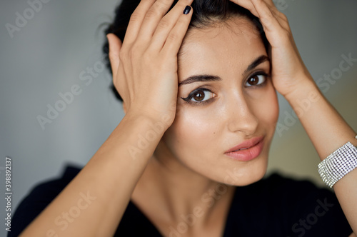 beautiful woman model touches her face with her hands on a gray background and evening dress decoration on her hand