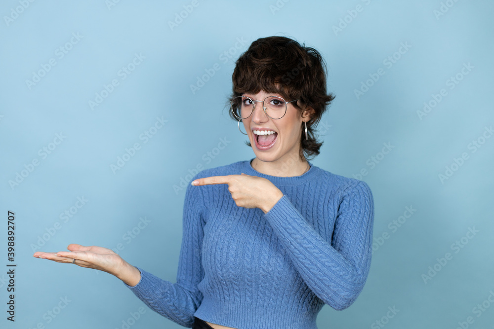 Young caucasian woman over isolated blue background surprised, showing and pointing something that is on her hand Young caucasian woman over isolated blue background surprised, showing and pointing something that is on her hand