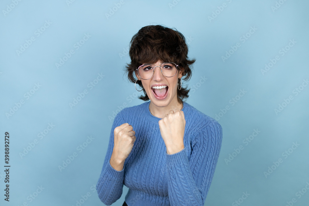 Young caucasian woman over isolated blue background very happy and excited making winner gesture with raised arms, smiling and screaming for success. Young caucasian woman over isolated blue background very happy and excited making winner gesture with raised arms, smiling and screaming for success.