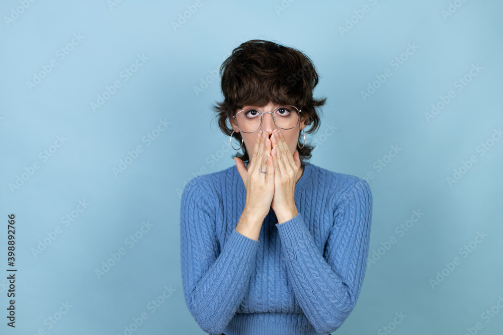 Young caucasian woman over isolated blue background with her hands over her mouth and surprised Young caucasian woman over isolated blue background with her hands over her mouth and surprised