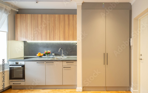 Modern interior of small kitchen in new apartment. Grey kitchen set with sink and oven. Wooden cabinets.