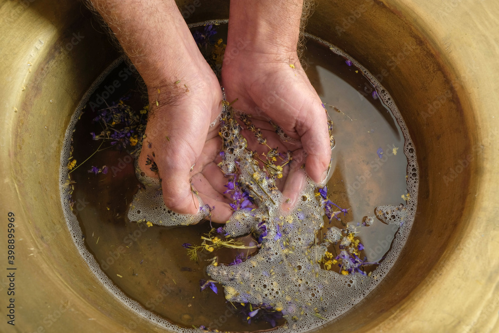 Flower bath in a copper bowl. Men's hands in the water. Water flower therapy. Top view. Copy space. Flower bath in a copper bowl. Men's hands in the water. Water flower therapy. Top view. Copy space.