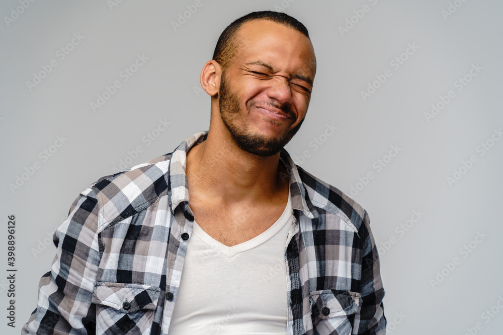 Photo of emotional young african-american man with eyes closed standing over light grey background Photo of emotional young african-american man with eyes closed standing over light grey background