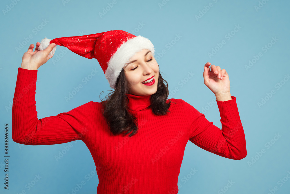 Beautiful brunette holding her santa hat on blue background Beautiful brunette holding her santa hat on blue background