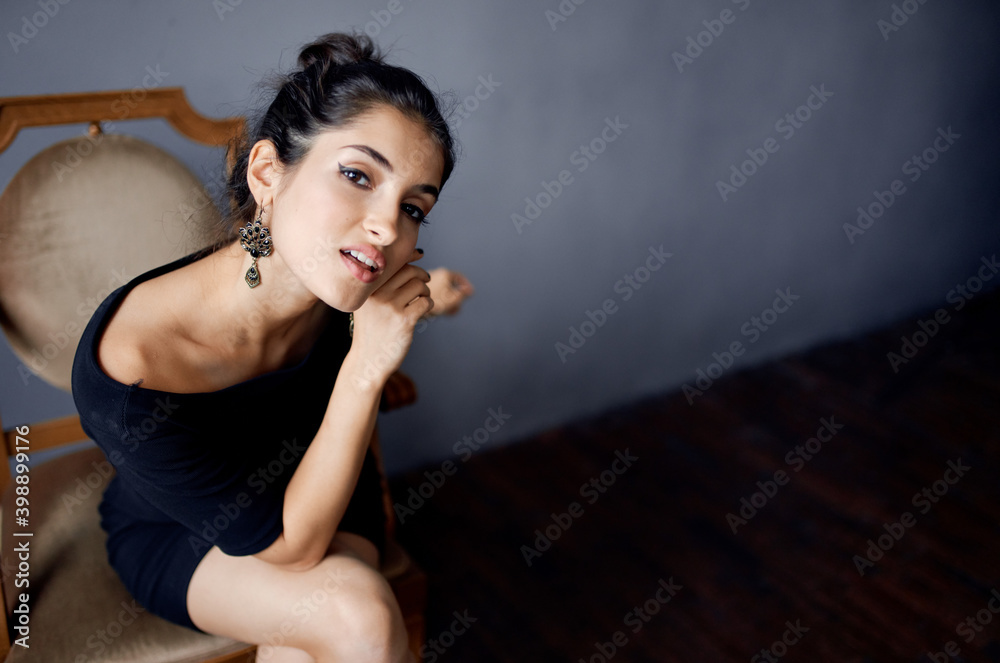 attractive brunette in black dress sits on a chair indoors and sexy appearance, earrings attractive brunette in black dress sits on a chair indoors and sexy appearance, earrings