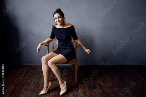 pretty woman sitting on a chair in a black dress room gray wall model hairstyle