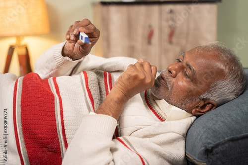 Foto Sick bed ridden old man seeing flu temperature on thermometer while sleeping at home