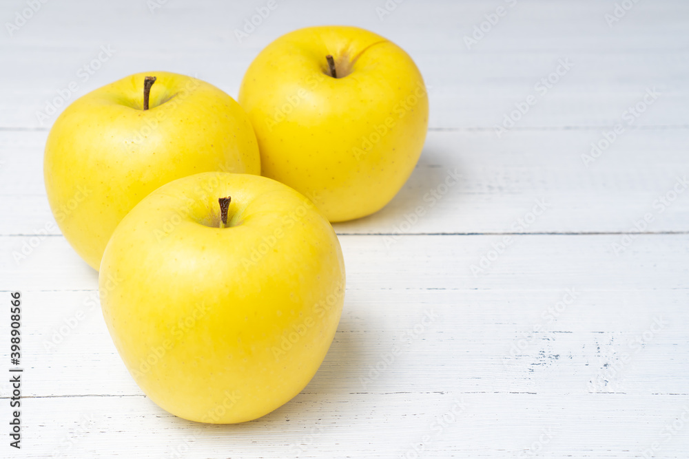 Three beautiful yellow ripe Golden apples on white wooden table. Sweet and juicy fruits.