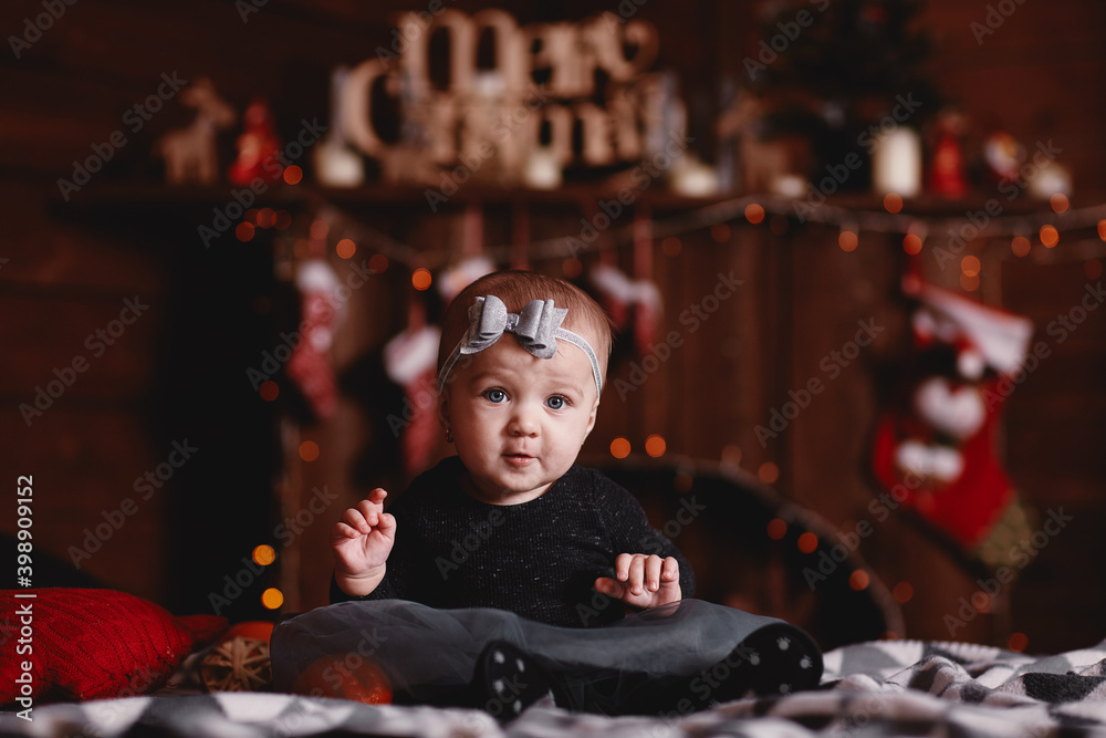 cute baby girl in dress and bow on head on bed with Christmas background behind.