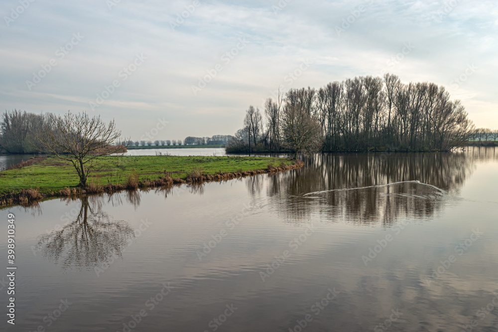 Φωτογραφία Bare tree silhouettes reflected in the mirror-smooth water surface of a wide creek in a Dutch nature reserve