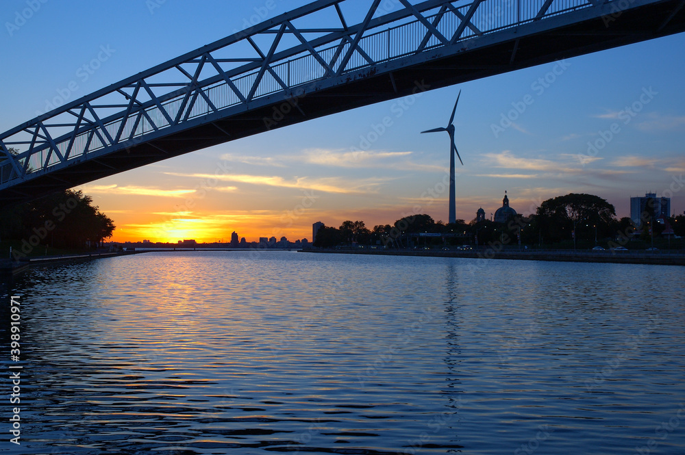 Sunset over water with wind turbine and foot bridge