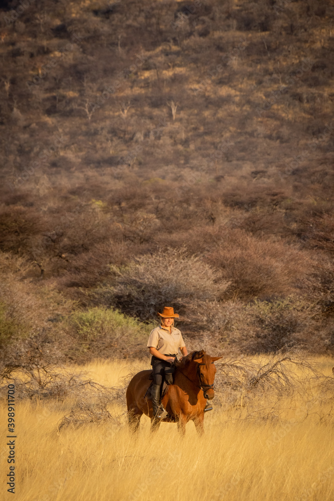 Blonde rides horse through grass near hillside Blonde rides horse through grass near hillside