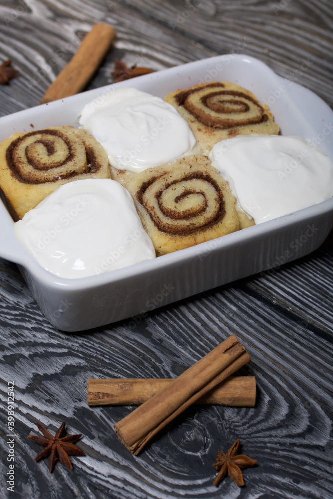 Baking cinnabons. The cinnamon rolls is in the baking dish. Next to it are cinnamon sticks and anise stars. On pine boards in black. Baking cinnabons. The cinnamon rolls is in the baking dish. Next to it are cinnamon sticks and anise stars. On pine boards in black.