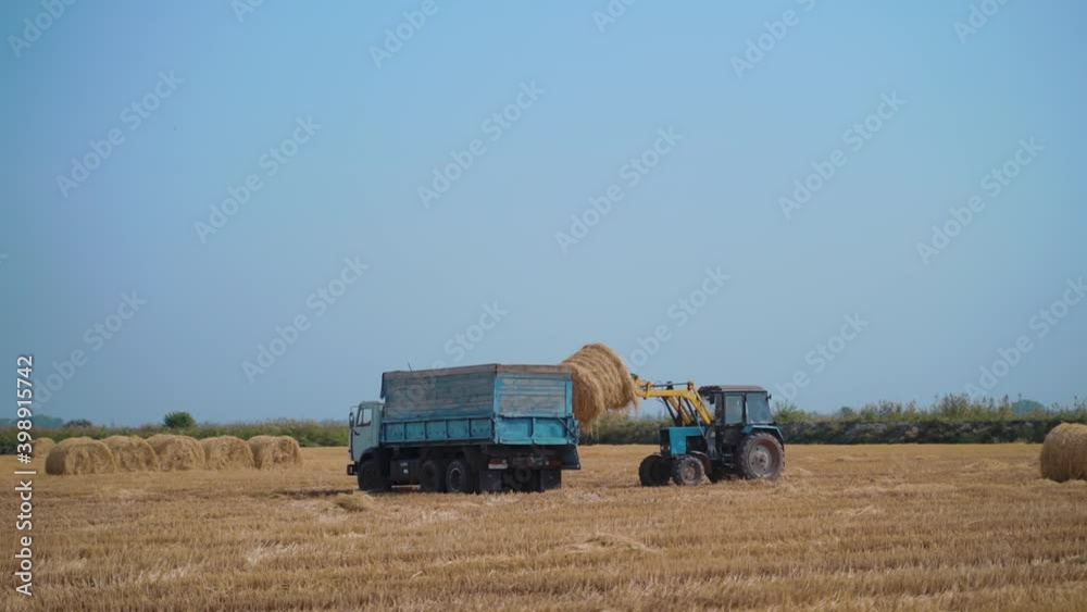 Tractor Machine Loading hay Bales on Truck Trailer during Agriculture Works Tractor Machine Loading hay Bales on Truck Trailer during Agriculture Works