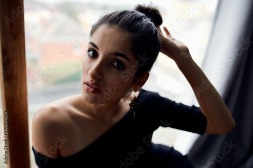 sexy woman near the window indoors with gray curtains in the background and evening dress makeup