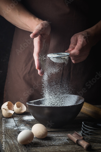 Quadro em tela Professional chef hands sifting flour in a bowl for cooking with baking utensils