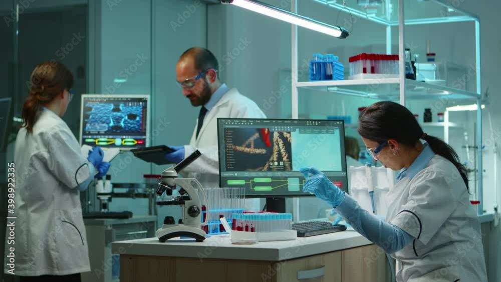 Scientist team checking virus development using high tech writing analysis results on computer in modern equipped lab at night. Doctors examining vaccine evolution with special tools for research.