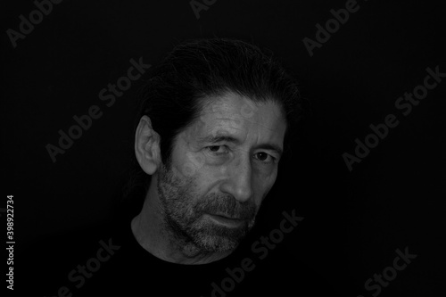 Black and white close-up portrait of bearded man with an critical and serious expression on dark black background. Front view portrait of thinking man. 