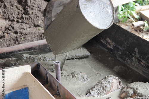 Pouring concrete from a bucket of the Foundation with wooden timbering of a village house