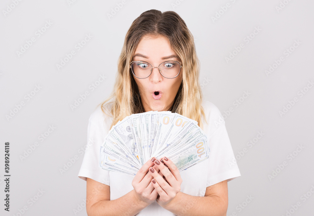 Young beautiful caucasian woman shocked by winning the lottery. The woman looks at the wad of cash she won. Young beautiful caucasian woman shocked by winning the lottery. The woman looks at the wad of cash she won.