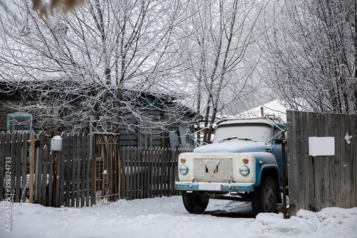 an old car stands behind a wooden fence in snowy siberia