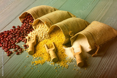 studio lighting. Retro style wooden background. There are cereals on it. Red beans, millet, pearl barley, sugar and a spice spoon next to it. Close-up
