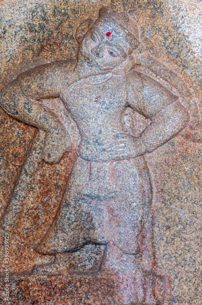 Hampi, Karnataka, India - November 4, 2013: Mural sculpture on brown-gray stone at Royal Enclosure. Closeup of mural sculpture of bearded man leaning on cane. Red dot on forehead.