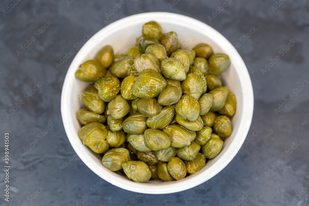 Pickled capers in a glass bowl on a dark background, top view close up (Turkish name; kapari) Pickled capers in a glass bowl on a dark background, top view close up (Turkish name; kapari)