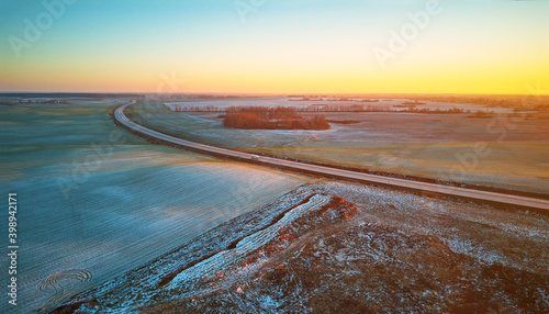 Obraz na płótnie Winter green Agricultural field winter crops under snow panorama. Highway December sunset Aerial scene. w salonie