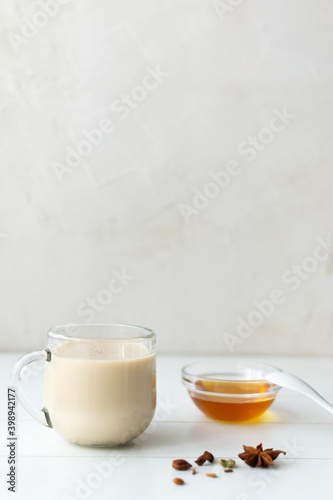 Masala tea in a glass cup with spices and honey on a white plate. Indian beverage. Vertical orientation. Copy space.