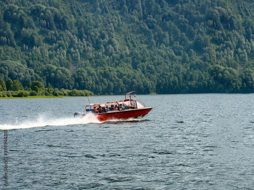 Fototapeta premium a red pleasure boat sails on the lake next to the mountain