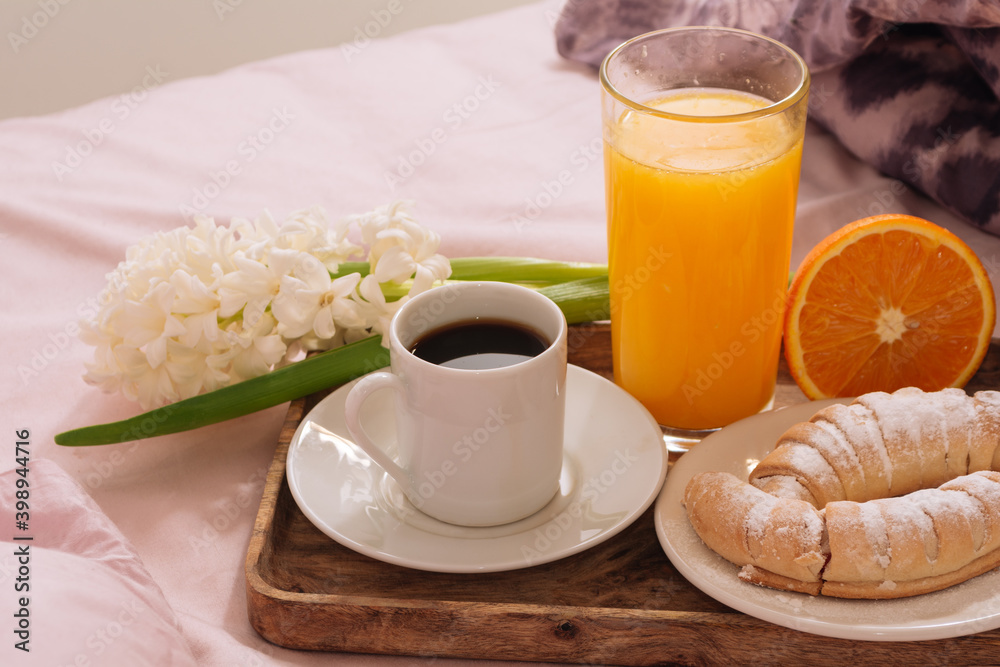 Breakfast in bed with hot coffee, powdered croissant, orange juice and fresh flowers white hyacinth on a wooden tray in pink-purple bedroom. Breakfast concept Breakfast in bed with hot coffee, powdered croissant, orange juice and fresh flowers white hyacinth on a wooden tray in pink-purple bedroom. Breakfast concept