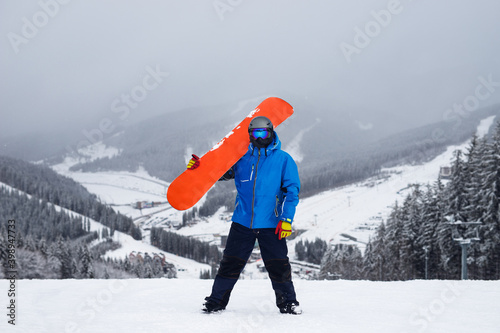 The guy hold on the shoulder orange snowboard in winter