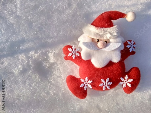 santa toy in red clothes with white snowflakes on the background of shadows on the snow