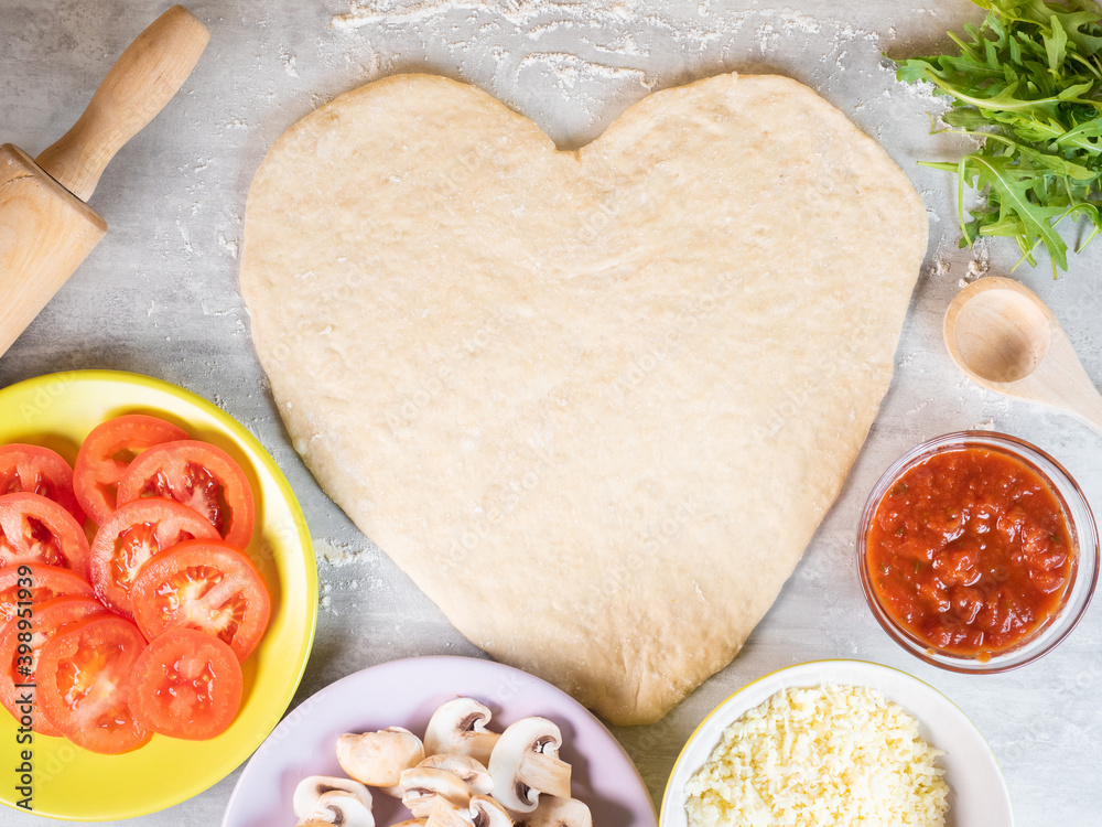 Heart shape pizza dough and ingredients on the table Heart shape pizza dough and ingredients on the table