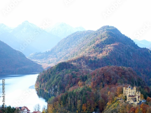 Panoramablick über das Gebiet von Schwangau mit Schloss Hohenschwangau umgeben von bunten Herbstwäldern und vor der Kulisse der bayerischen Alpen.