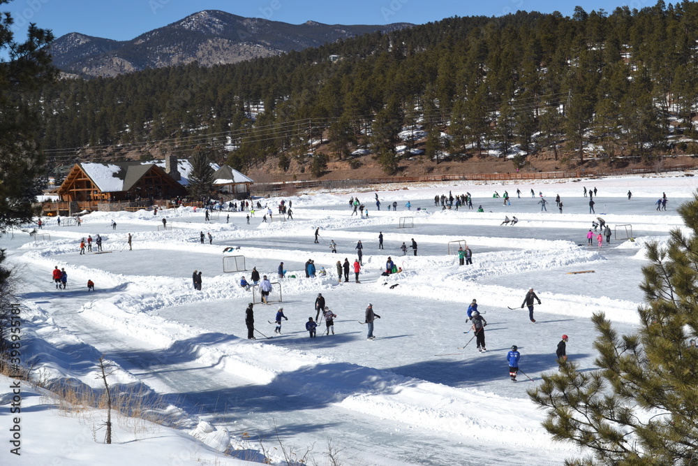 Ice skating and ice hockey on a frozen lake ice rink with a mountain view in Evergreen, Colorado