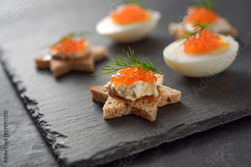 Star shaped canapes and halved eggs with red caviar and dill garnish on a dark slate plate for a festive holiday buffet