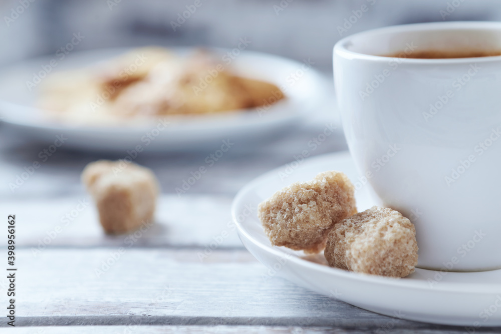 Cup of coffee and brown sugar cubes ( focus on sugar) on bright wooden background. Close up. Cup of coffee and brown sugar cubes ( focus on sugar) on bright wooden background. Close up.