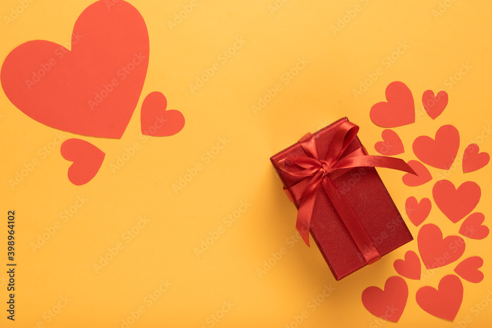red box with satin ribbon on yellow background. Many red hearts of different sizes. Valentine's day holiday.