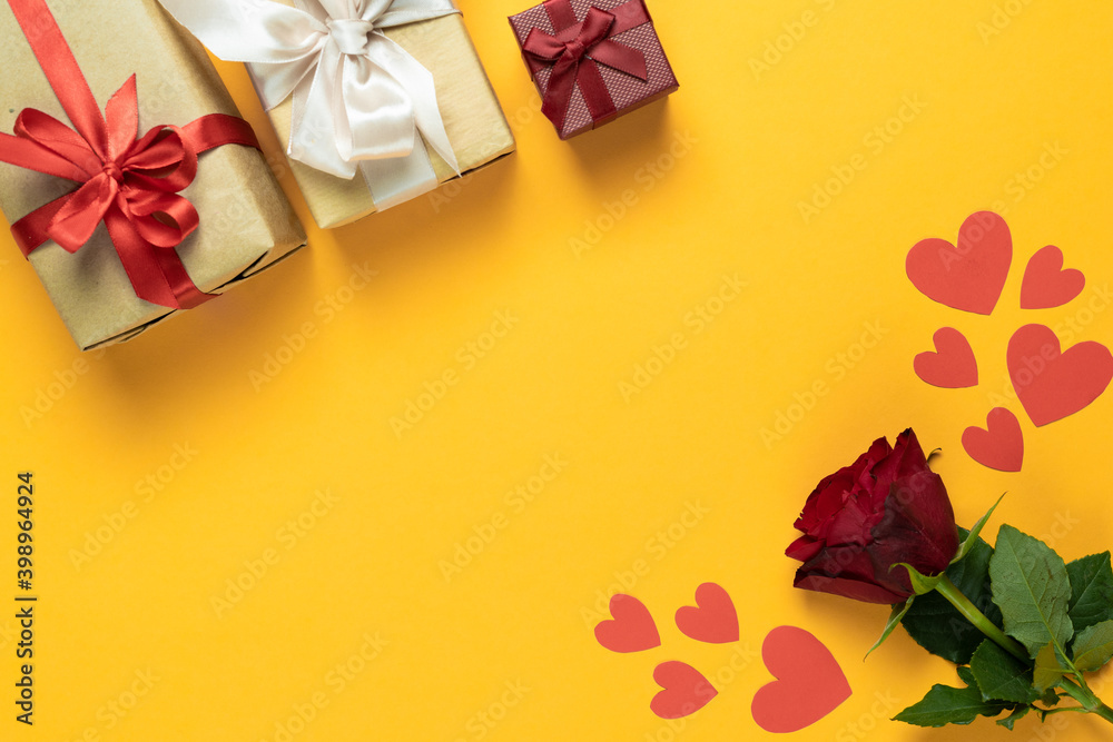 top view on a yellow background lies a red rose near the packed boxes with gifts. Hearts made from cardboard. . valentine's day concept