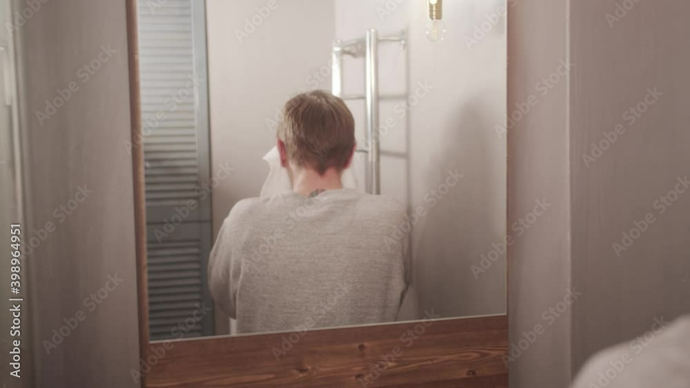An adult man in the bathroom has brushed his teeth, washed, and is wiping his face and hands dry with a white towel. An adult man in the bathroom has brushed his teeth, washed, and is wiping his face and hands dry with a white towel.